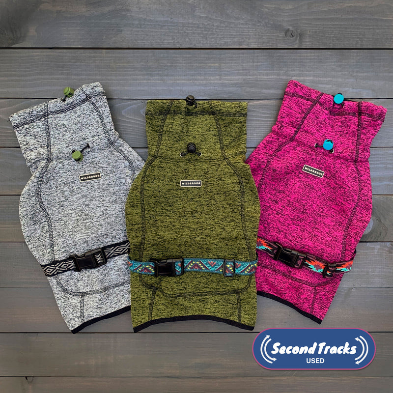 Three (Used) Fleece Jackets for dogs in gray, green, and a surprise color with adjustable belts and clasps are displayed on a wooden surface. The Second Tracks Used logo is visible in the bottom right corner.